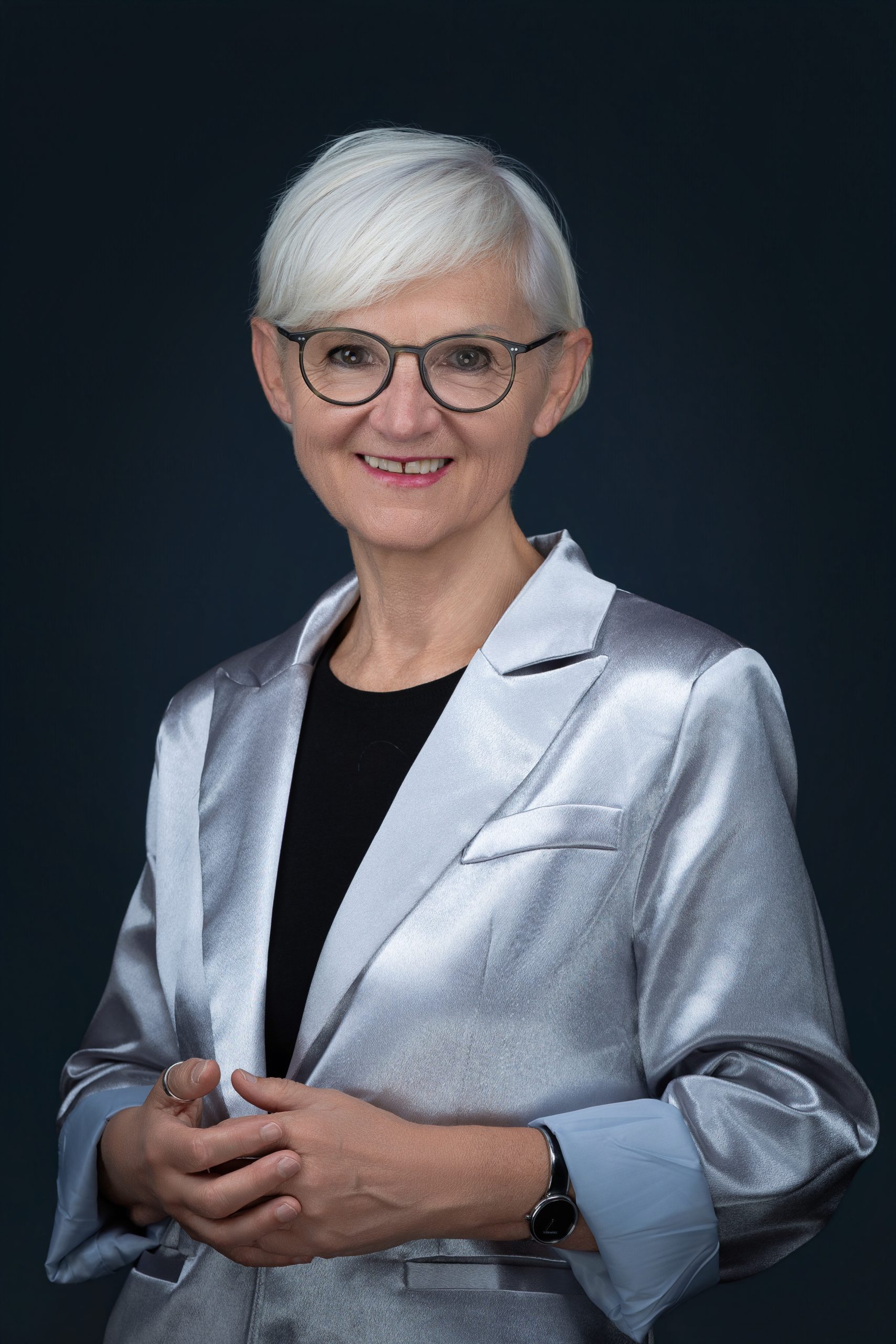 Porträtfoto von Mag.a Maria Rösslhumer, Gründerin von StoP in Österreich, lächelnd vor neutralem, dunklem Hintergrund.